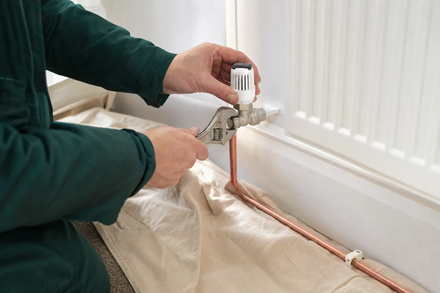 Hands fitting a thermostatic valve to a radiator over a dust sheet