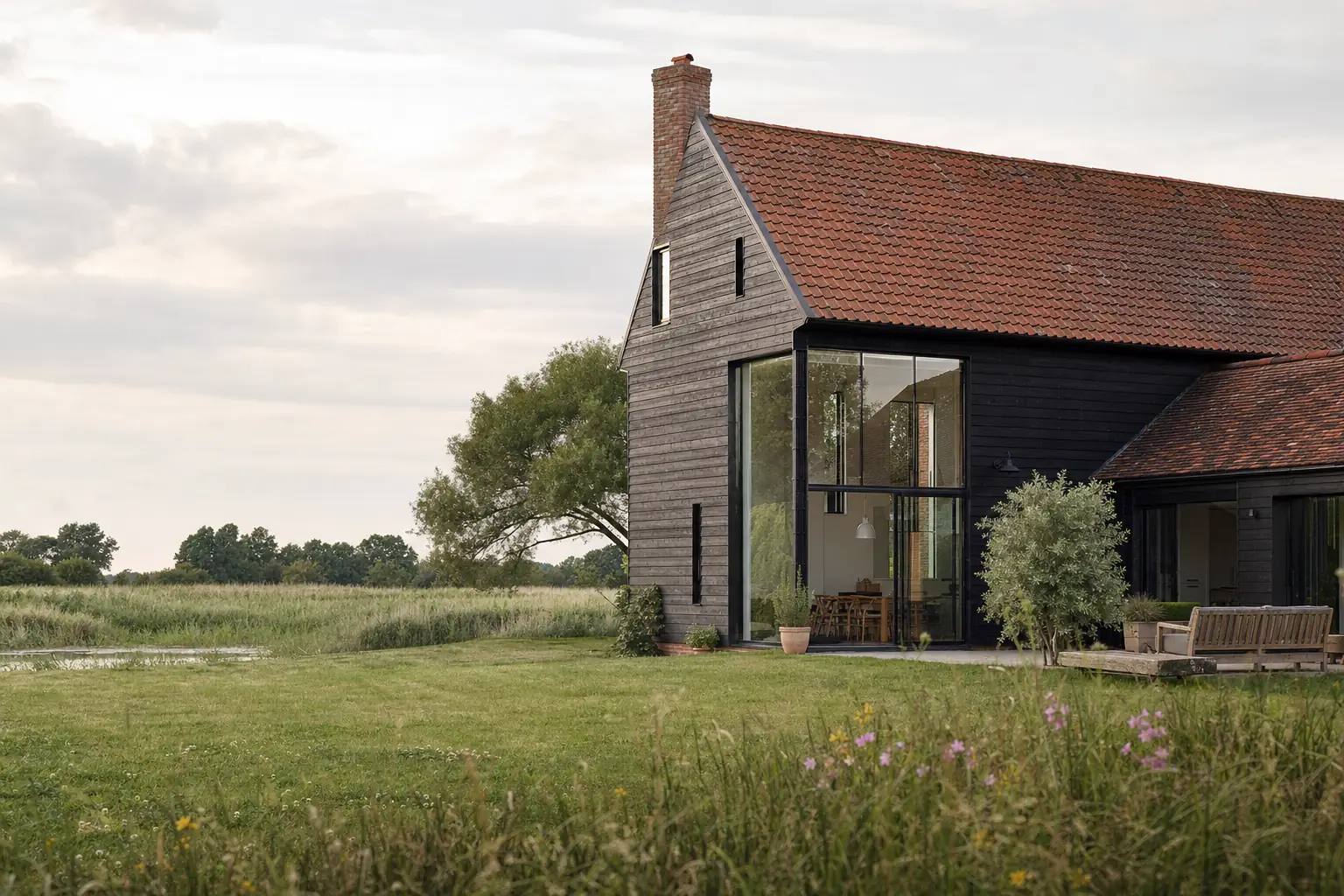 Black weatherboarded barn conversion with a full-height glazed opening beside reed beds