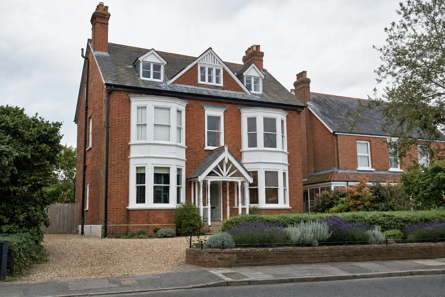Red-brick Victorian villa with white two-storey bay windows and a lavender front garden