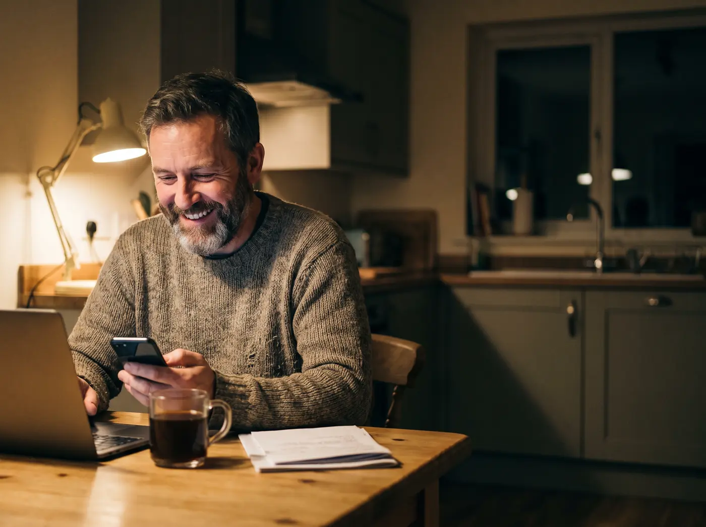 A business owner at his kitchen table, smiling at replies arriving on his phone